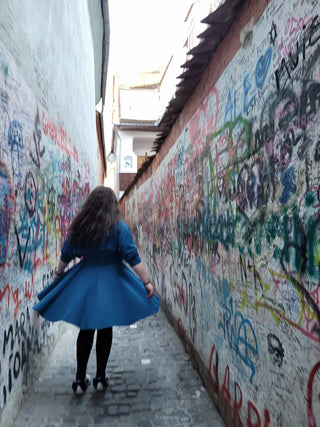 Corina wearing the Blanche dress by Cori Tailor, walking through the graffiti-covered Strada Sforii in Brașov, Romania.