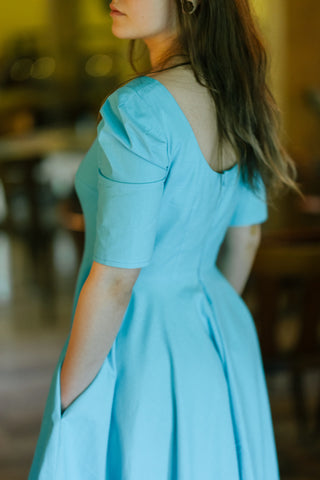 Close-up of the Bubbles Dress by Cori Tailor — showcasing puff sleeve, scoop back, and soft pleats in light blue cotton fabric

