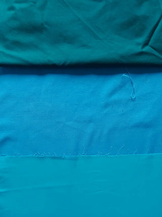 Close-up of three cotton fabric swatches in teal, turquoise, and aquamarine, representing the colorful palette behind Cori Tailor’s handmade garments.
