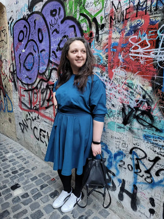 Corina wearing the Blanche Dress on Strada Sforii in Brașov, Romania – a handmade teal fit-and-flare dress, styled with sneakers and a black backpack.