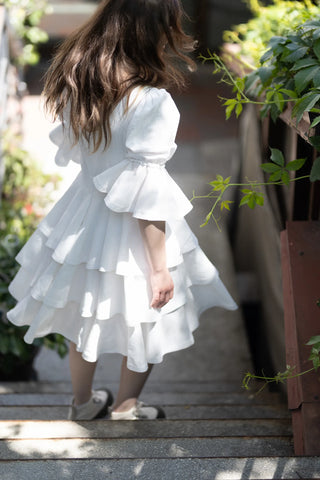 Back view of the Freya Dress by Cori Tailor, featuring flowing tiered skirt and puff sleeves, model walking down sunlit stairs
