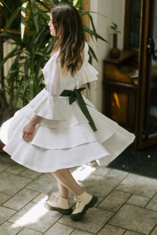 Model spinning in the Freya Dress by Cori Tailor, side view with layered skirt in motion and green bow sash, captured indoors