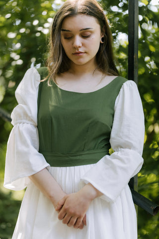 Front close-up of Heidi Dress showing green bodice with scoop neckline and white gathered sleeves, model standing with hands folded.