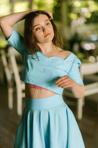 Close-up of the Jasmine Set featuring a sweetheart neckline crop top and high-waisted skirt in turquoise cotton, model posed indoors with arm raised.