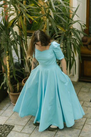 Model wearing the Jasmine Set — sweetheart neckline crop top and full circle maxi skirt in turquoise cotton — photographed in an indoor garden setting.