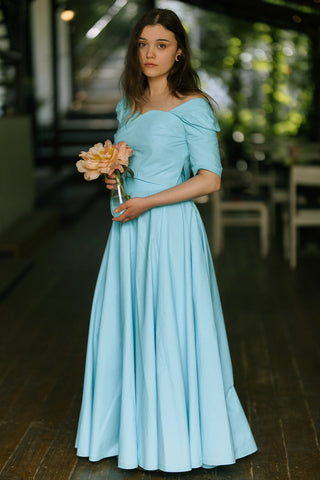 Woman posing in the Jasmine Skirt by Cori Tailor — turquoise cotton skirt with full volume and fitted waist, holding a peach flower outdoors on the terrace of Acaju cafe in Iași