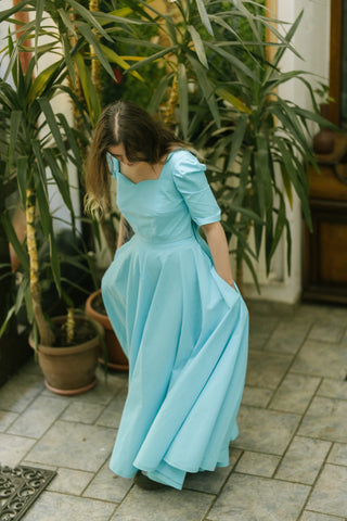 Woman twirling in the Jasmine Skirt by Cori Tailor — flowing turquoise cotton skirt with full volume, captured in motion outdoors among potted plants