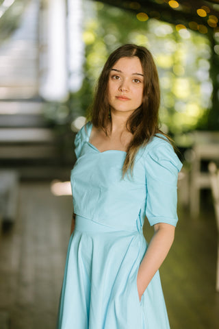 Woman wearing the Jasmine Top by Cori Tailor — turquoise cotton crop top with sweetheart neckline and puff sleeves, photographed outdoors on the terrace of Acaju cafe in Iași