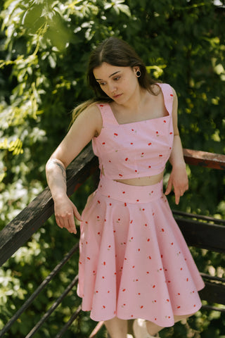 Model wearing Lolita cherry pink gingham set, leaning on railing outdoors — Cori Tailor summer handmade clothing.