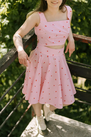 Front view of the Lolita Skirt by Cori Tailor, pink gingham pattern with small cherry print, worn with matching crop top, photographed outdoors