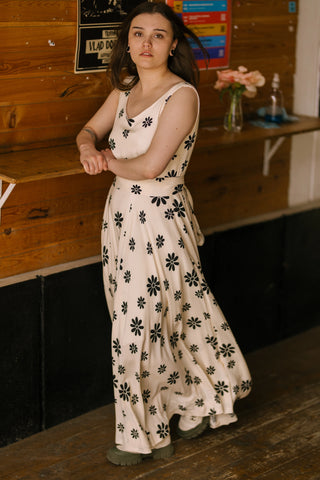 Model leaning casually against a wall, wearing the Penny Lane Dress — sleeveless floral-print maxi dress.
