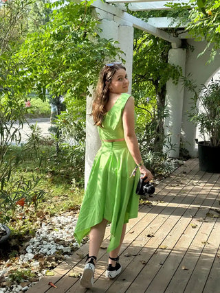 Woman wearing the Tinkerbell Deux Pièces green two-piece outfit walking on a wooden path with a vintage camera in hand – handmade design by Cori Tailor